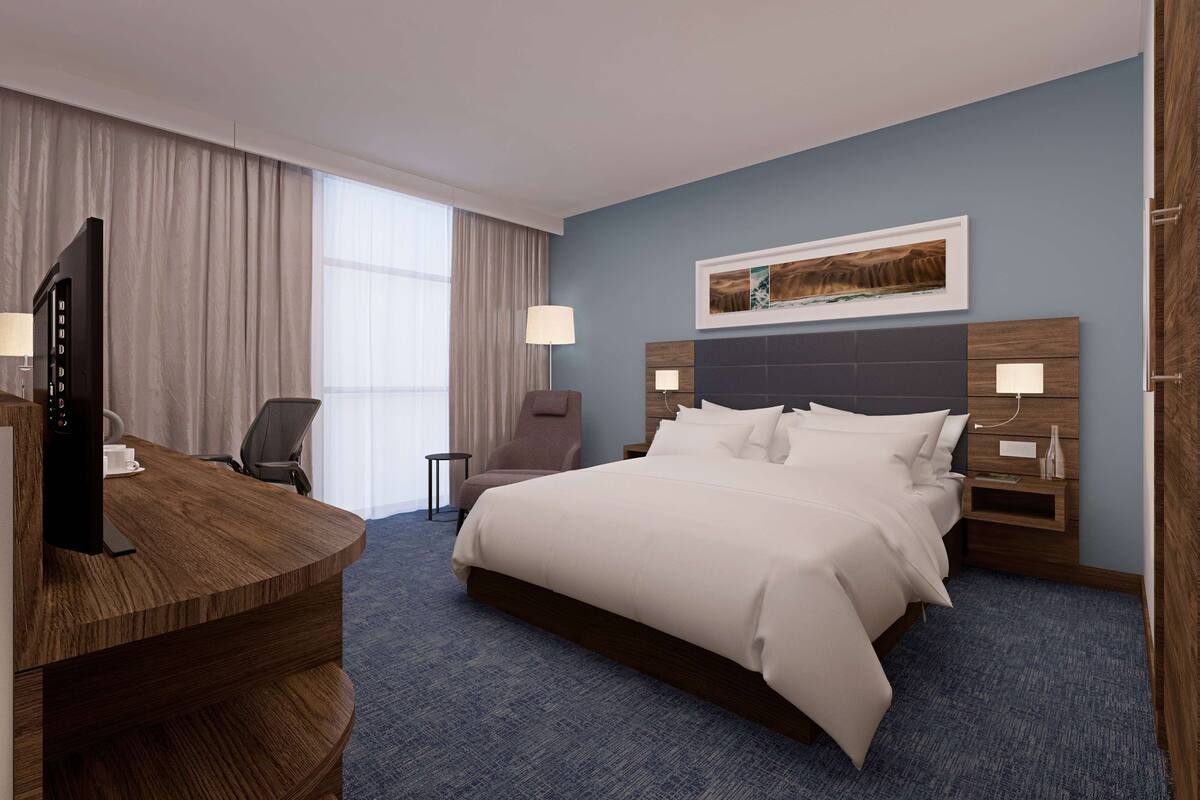 A hotel room with a bed, a desk, a chair, a TV, and a window with curtains.