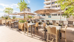 An outdoor patio area with tables and chairs, umbrellas, and a pool in the background. - Hilton Garden Inn Windhoek (Windhoek)