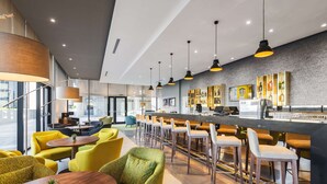 A modern bar area with high stools, a counter, and a seating area with yellow chairs and a round table. - Hilton Garden Inn Windhoek (Windhoek)