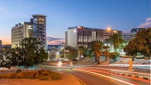 A modern hotel with a circular tower, a flat-roofed building, and a sign indicating a bus stop. - Hilton Garden Inn Windhoek (Windhoek)