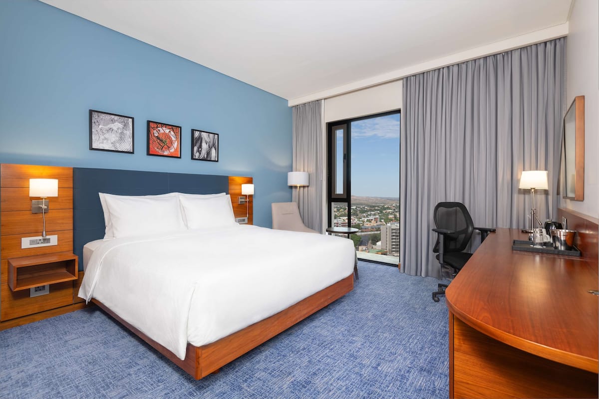 A hotel room with a large bed, a desk, and a view of the city.