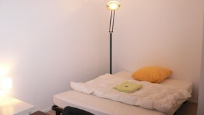 Une petite chambre avec un lit simple, une table de chevet, une lampe et un lampadaire.