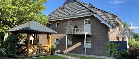 Une maison à deux étages avec un balcon, un belvédère en bois et une pelouse bien entretenue.
