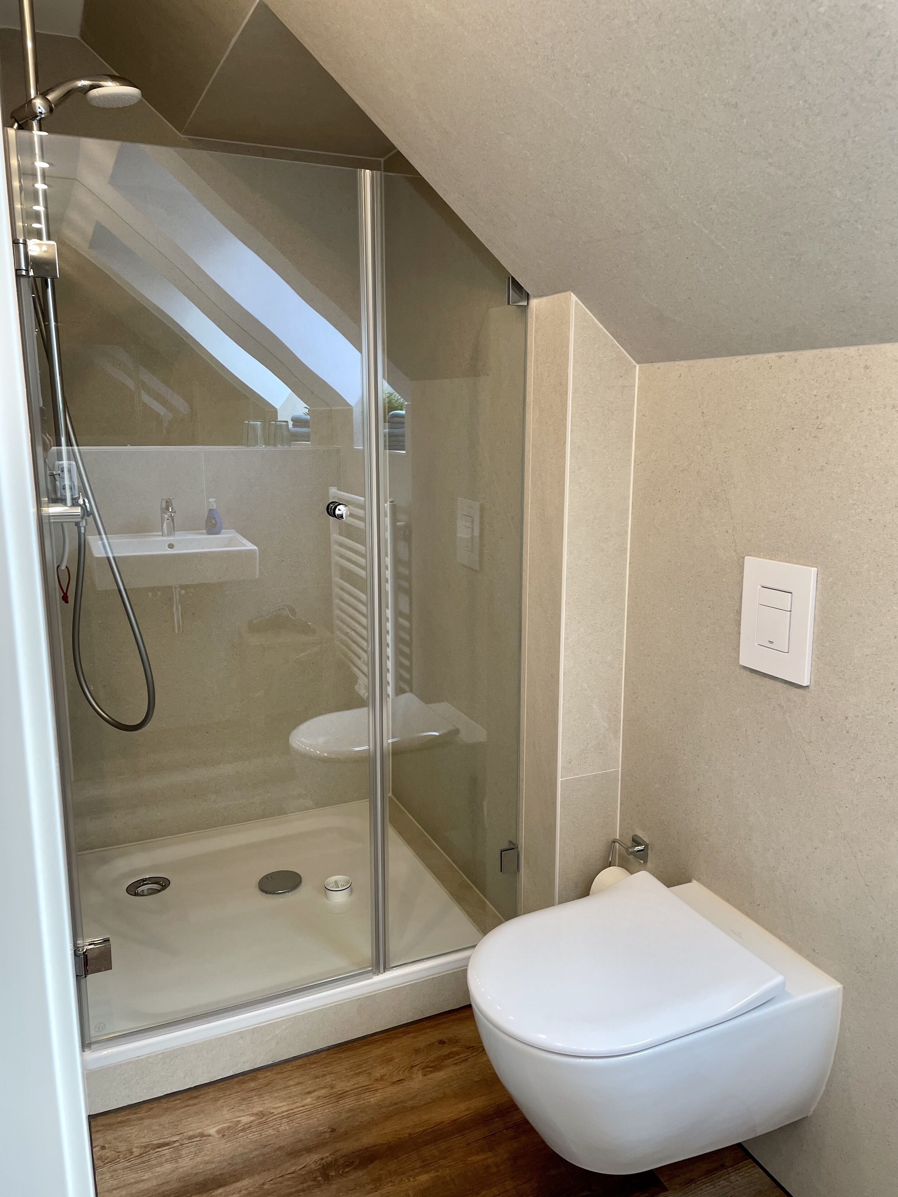 Une salle de bain moderne avec une douche à parois de verre, des toilettes blanches et un petit lavabo.