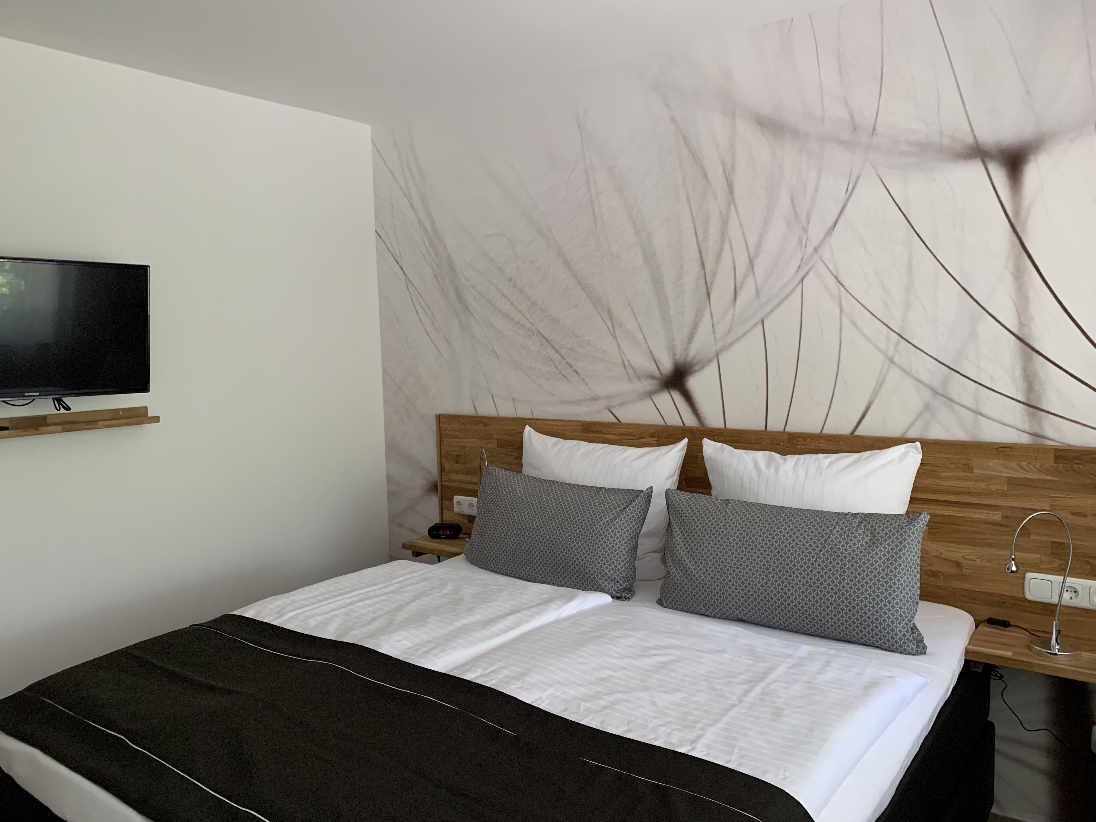 Una cama bien tendida con un cubrecolcha negro, cabecera de madera y televisor montado en la pared.