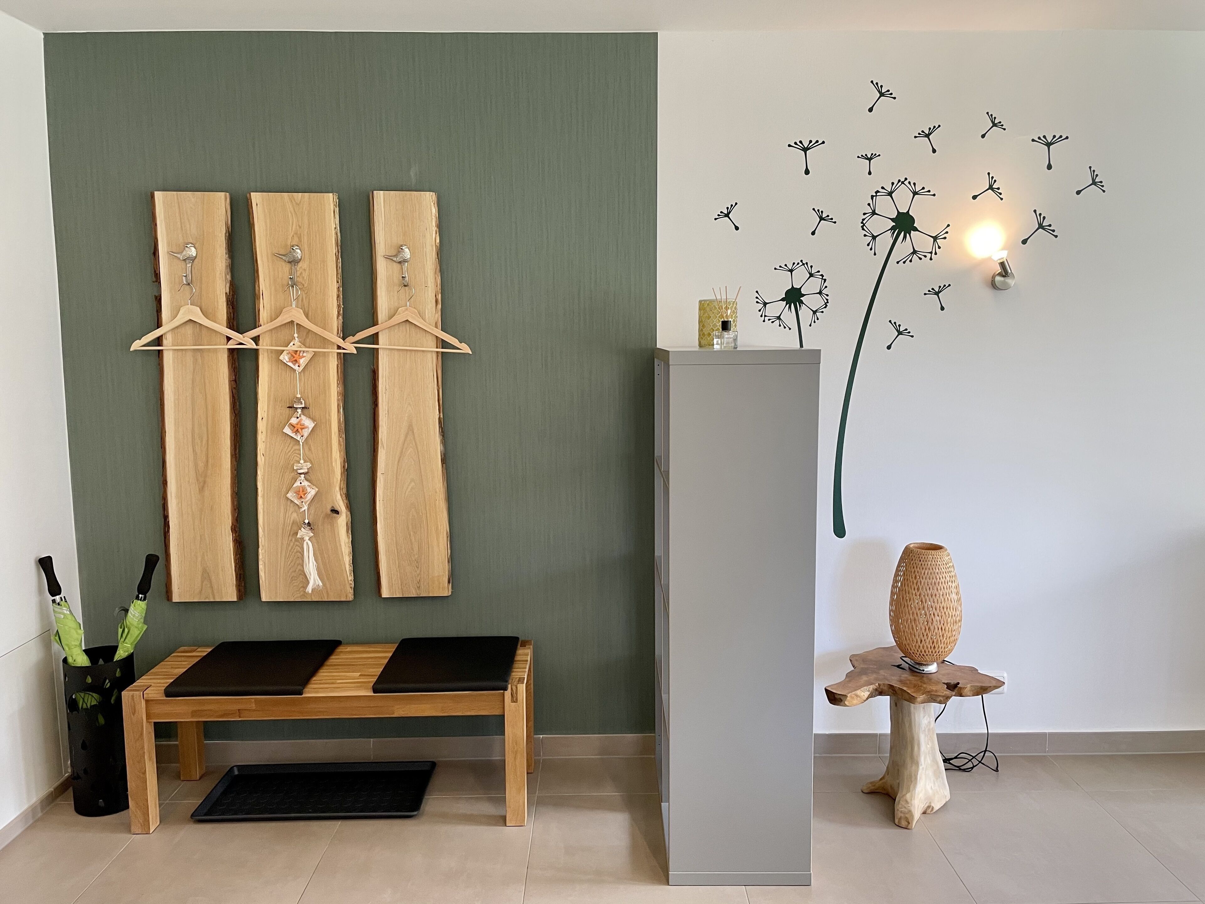 A room with a wooden bench, a grey cabinet, and a wall decoration of birds and dandelions.