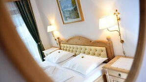 A hotel room with a large bed, two bedside tables, a wooden headboard, and two wall-mounted lamps. - Garni Wildbach (Selva di Val Gardena)