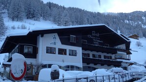 A hotel with a snow-covered exterior, a sign reading "Garni Wildbach," and a view of a snowy mountain in the background. - Garni Wildbach (Selva di Val Gardena)