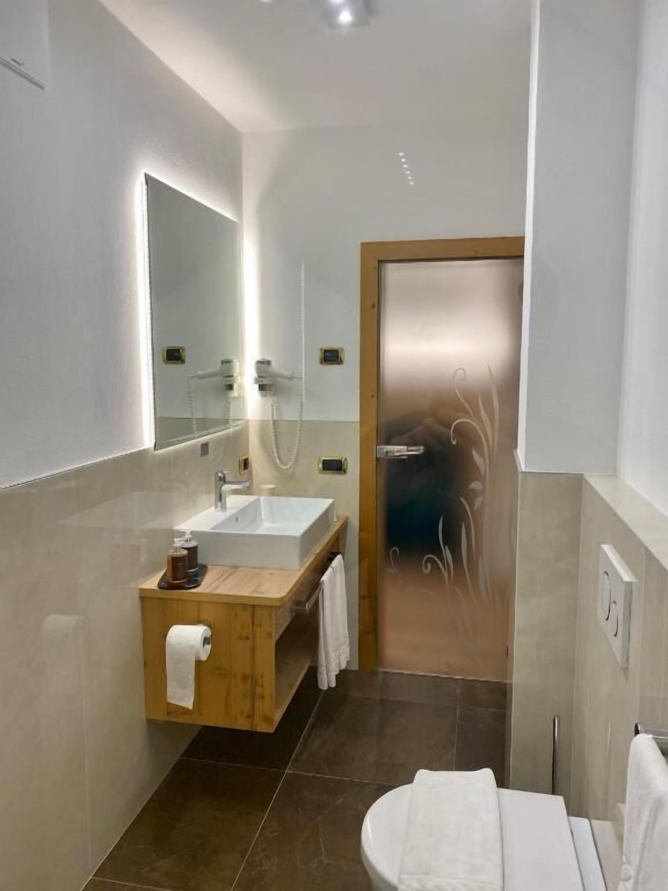 Une salle de bain moderne avec un grand miroir, un lavabo blanc et une cabine de douche en verre.