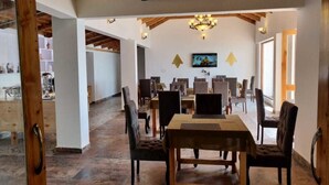 A spacious dining area with a high ceiling and wooden beams, featuring a central table surrounded by chairs. - Parwati Retreat (Ranikhet)