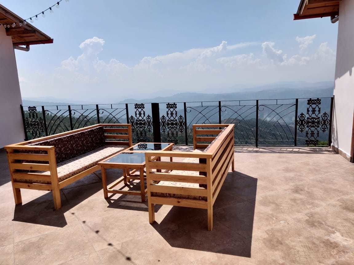 Un balcon doté de mobilier en bois, d’une table en verre et offrant une vue sur des montagnes lointaines.