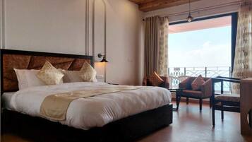 A large bed with a wooden headboard and multiple pillows, a bedside lamp, and a view of a balcony with a chair.