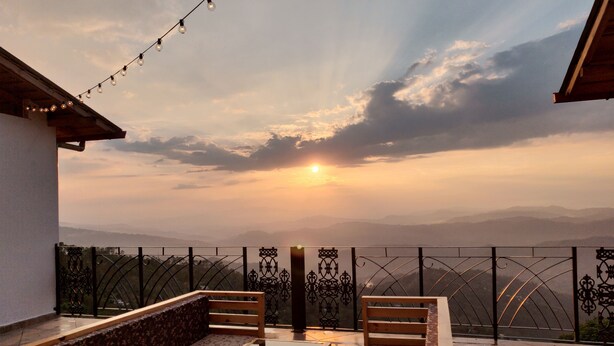 A balcony with a wooden bench and table, overlooking a mountainous landscape during sunset. - Parwati Retreat (Ranikhet)