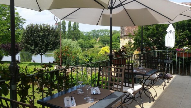 An outdoor patio with tables and chairs, a view of a lake, and surrounding greenery. - Hotel Coté Rivage (Badefols-sur-Dordogne)