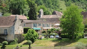 A riverside building with stone walls, a small garden, and a parked car. - Hotel Coté Rivage (Badefols-sur-Dordogne)