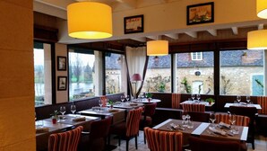 A restaurant with multiple tables and chairs, large windows with curtains, and hanging yellow lamps. - Hotel Coté Rivage (Badefols-sur-Dordogne)