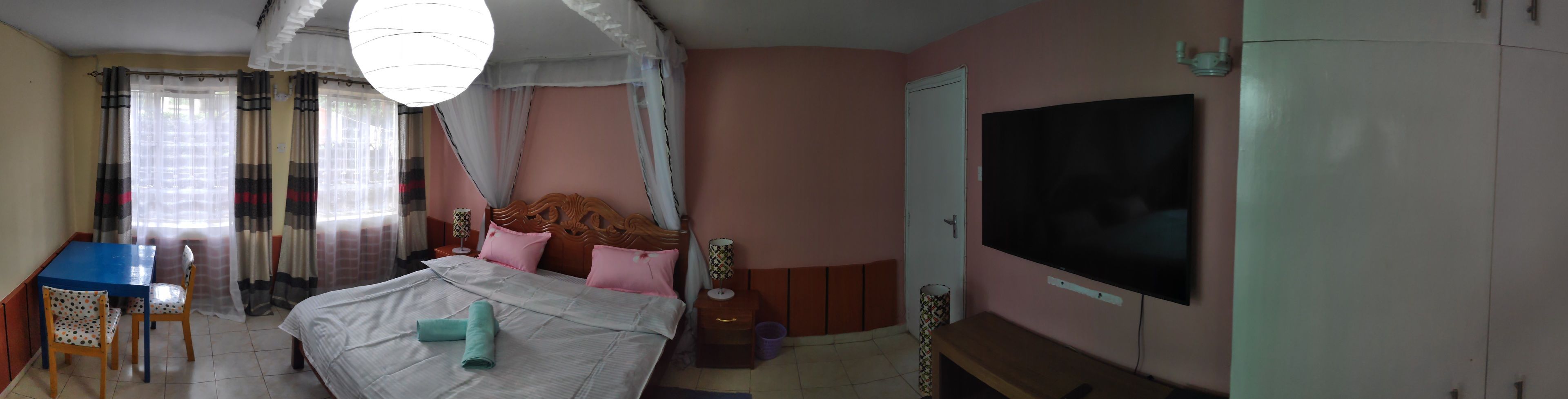 Una habitación con cama, televisión, mesa y sillas, y ventana con cortinas.
