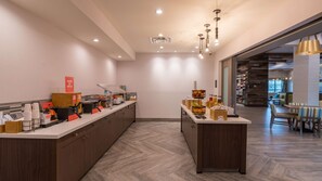 A modern hotel lobby with a long reception desk, a coffee station, and a seating area with tables and chairs.
