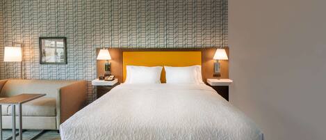 Une chambre d’hôtel avec un grand lit, deux tables de chevet avec des lampes, un petit canapé et un mur décoré d’un motif.