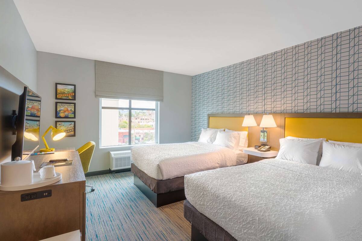 Une chambre d’hôtel avec deux lits, un bureau avec une lampe, une télévision et des tableaux encadrés au mur.