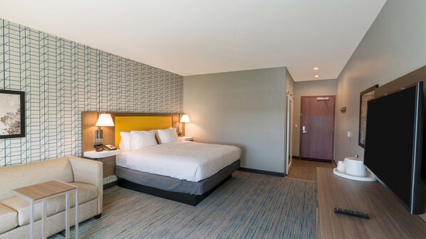 A hotel room with a bed, bedside tables, a TV, a sofa, and a patterned wall. - Hampton Inn Riverside Downtown Convention Center (Riverside)