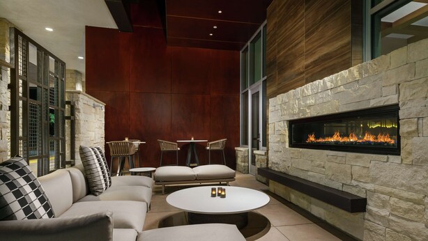 A modern outdoor seating area with a stone fireplace, cushioned seating, and a round table. - Hilton Garden Inn Sunnyvale (Sunnyvale)