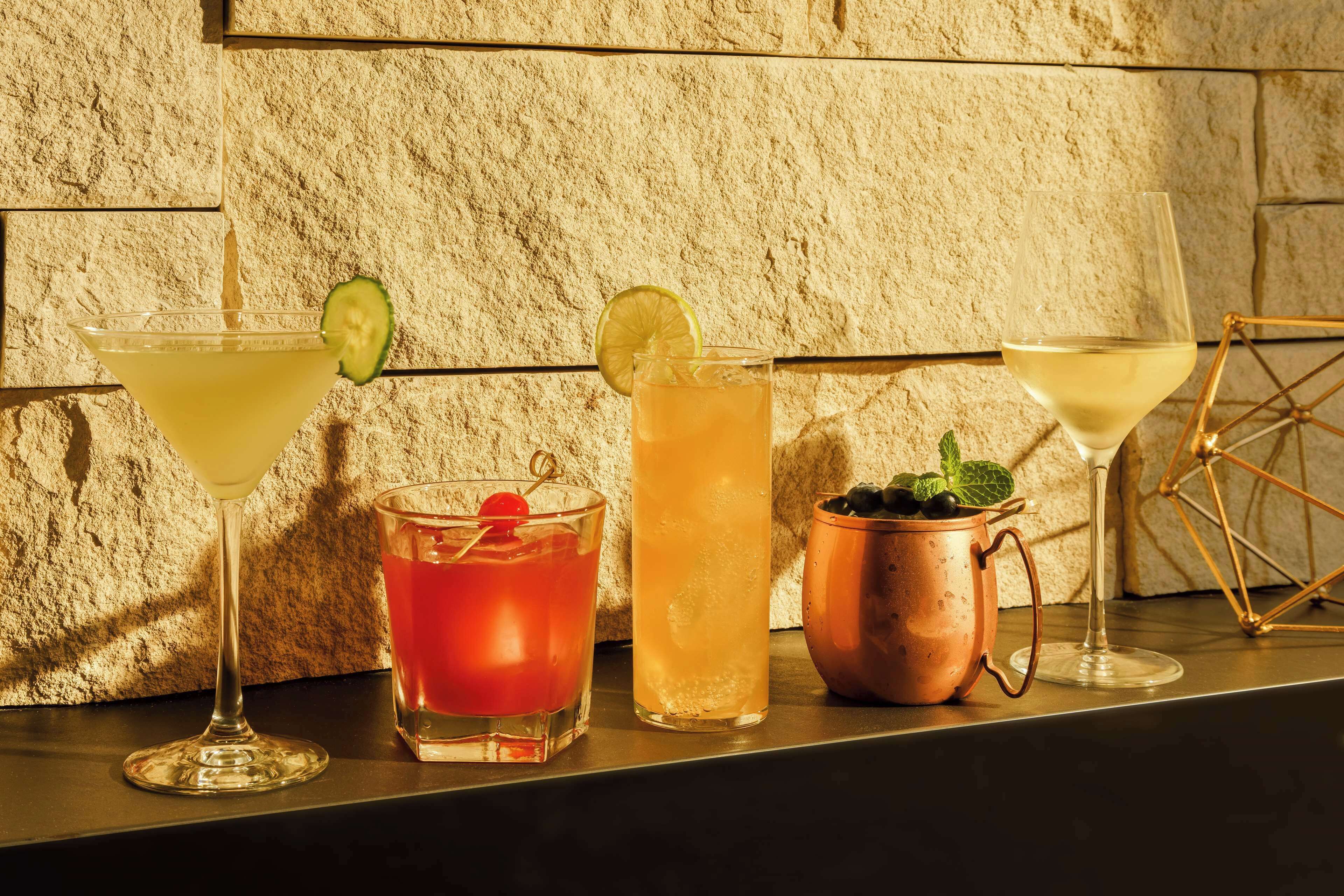 Four different types of drinks on a bar counter with a textured stone wall in the background.