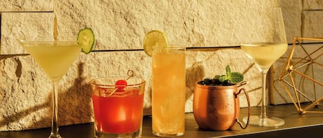 Four different types of drinks on a bar counter with a textured stone wall in the background.