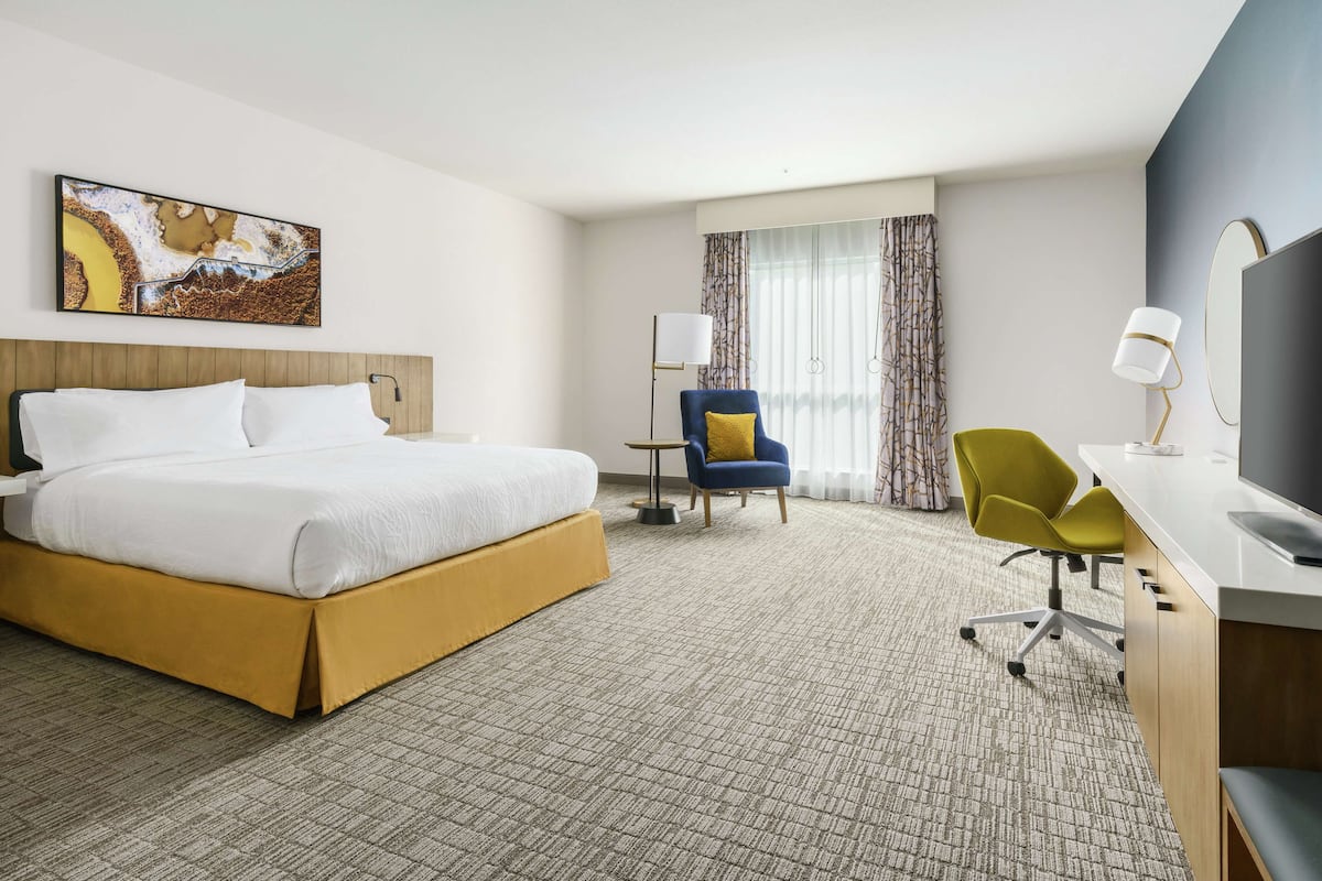 A hotel room with a large bed, a desk with a chair, a television, and a painting on the wall.
