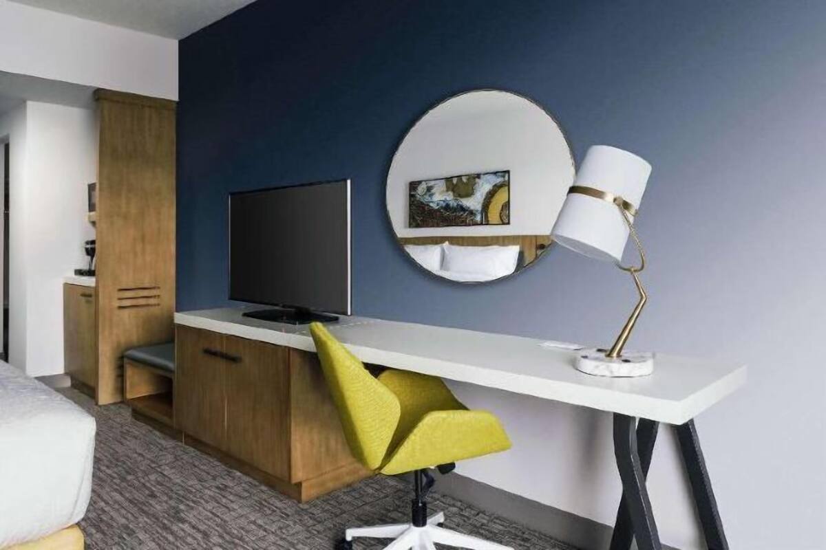A hotel room with a bed, a desk with a chair, a television, a lamp, and a mirror.