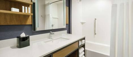 A modern bathroom with a large mirror, a sink, and a bathtub. There are shelves with toiletries and towels.