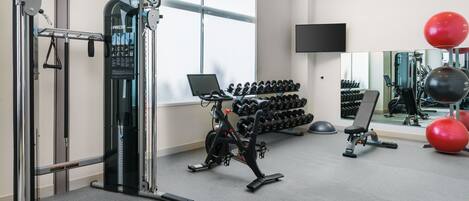 Un gimnasio con equipo de ejercicio, mancuernas y una televisión en la pared.