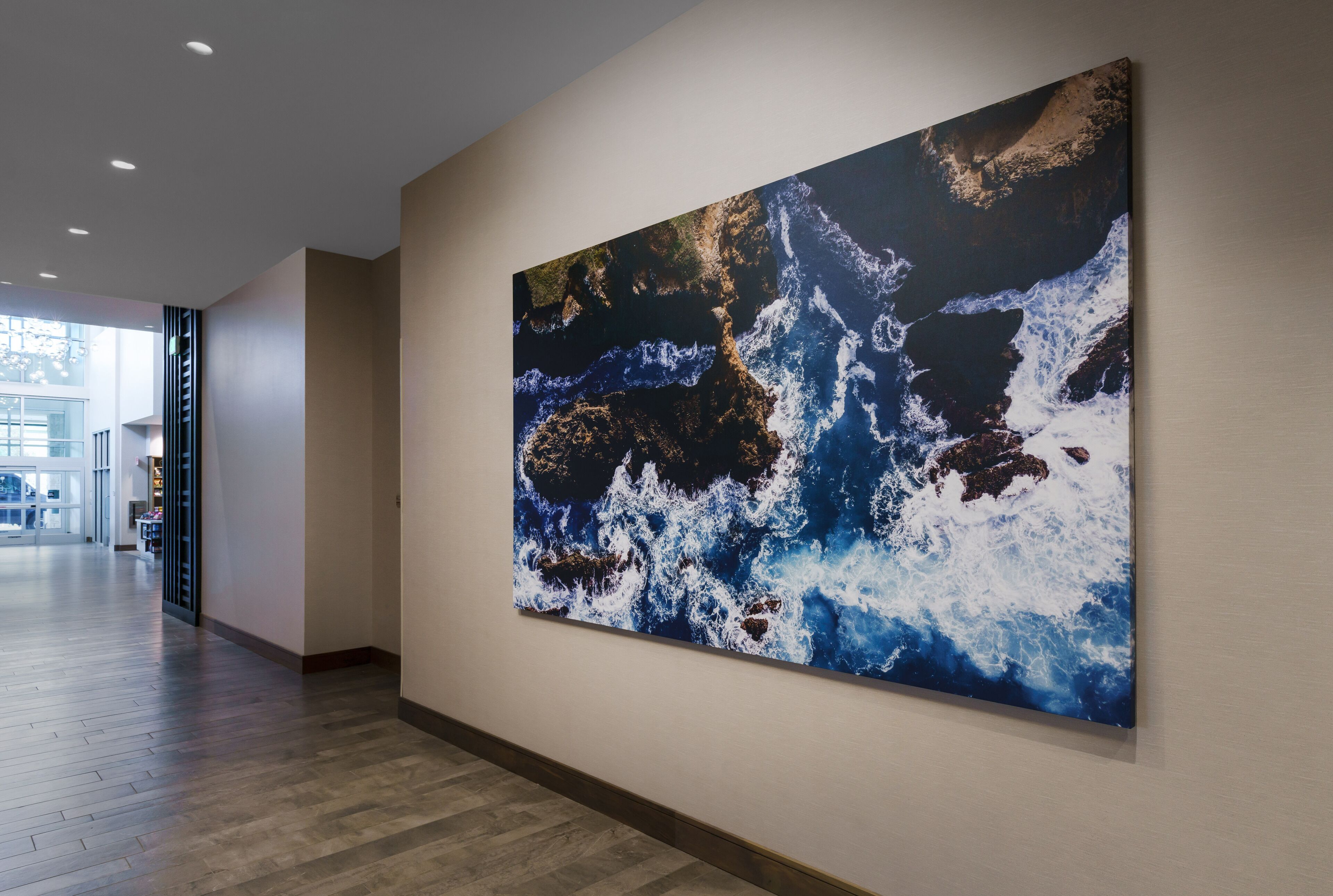 A hallway with a large abstract painting on the wall, wooden flooring, and a view of the outdoors through a glass door.