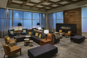 A modern hotel lobby with a sectional sofa, armchairs, a flat-screen TV, and a wooden accent wall.
