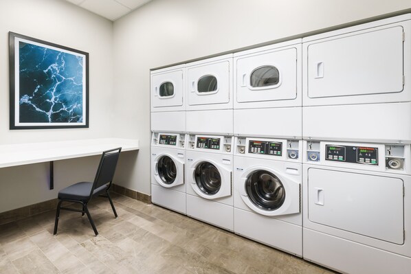 A laundry room with multiple washing machines, a chair, and a framed picture on the wall.
