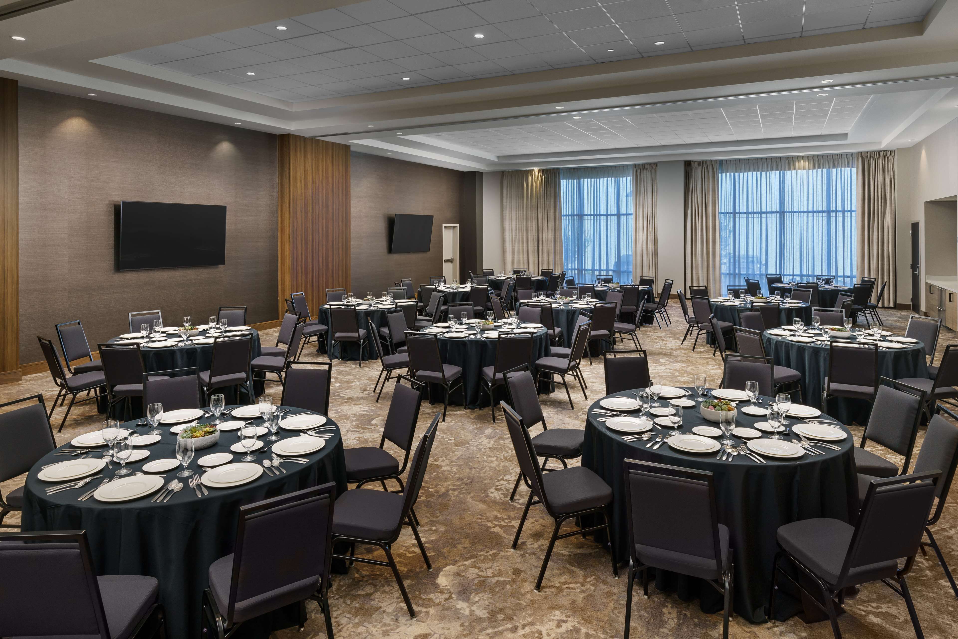A conference room with multiple round tables, each set with chairs, plates, and cutlery.