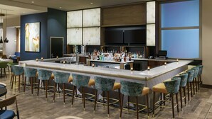 A bar area with a long counter, multiple stools, and a variety of bottles. - Hilton Garden Inn Sunnyvale (Sunnyvale)