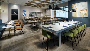 A modern restaurant with multiple dining areas, including a central long table and several smaller tables. - Hilton Garden Inn Sunnyvale (Sunnyvale)