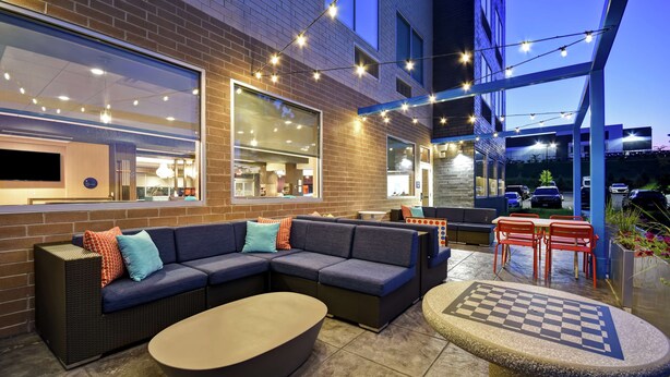 An outdoor seating area with a sofa, ottoman, and a chess table. - Tru By Hilton Cincinnati Airport South Florence (Florence)