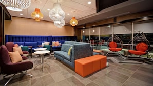 A modern lounge area with a blue sofa, orange ottoman, and hanging chairs. - Tru By Hilton Cincinnati Airport South Florence (Florence)