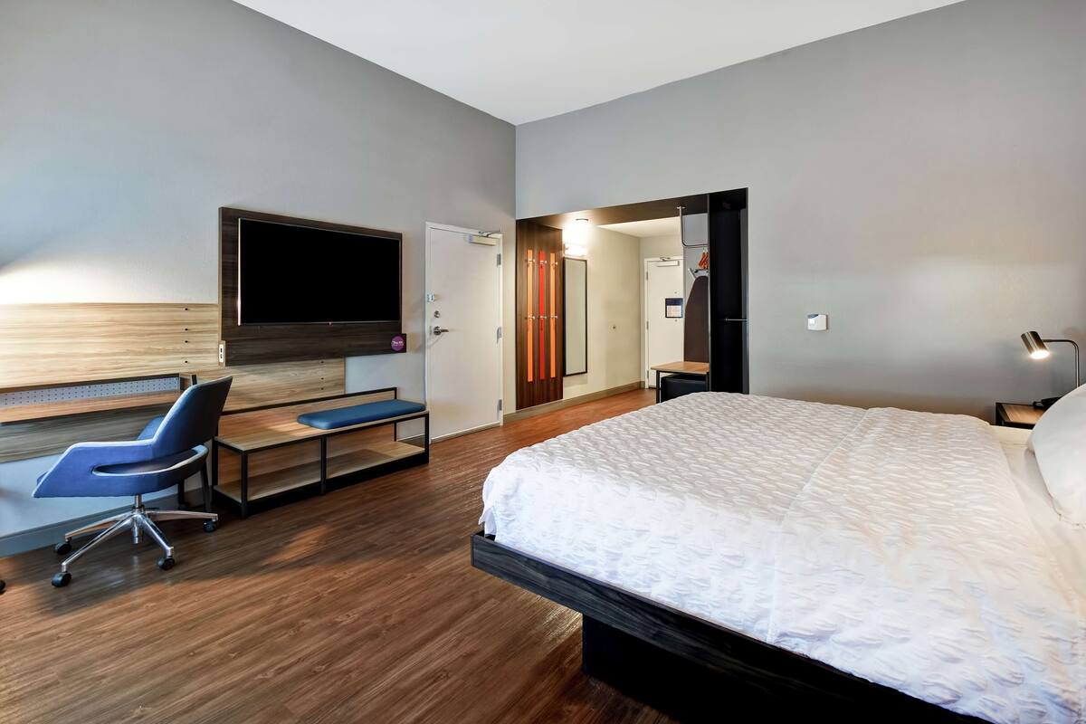 Una habitación de hotel moderna con una cama grande, un escritorio con una silla, un televisor de pantalla plana montado en la pared y un vestidor.