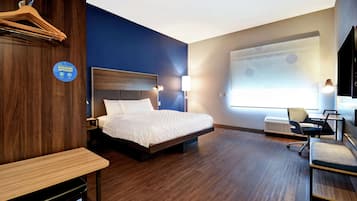 A hotel room with a bed, desk, chair, and a projector screen on the wall.