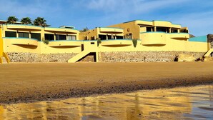 Un bâtiment situé sur la côte, à plusieurs étages, avec des fondations en pierre et un ciel dégagé.