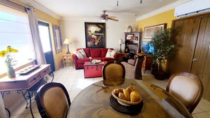 Un coin repas avec une table dressée pour deux personnes, un canapé rouge, un téléviseur et un ventilateur de plafond.