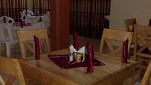 A dining area with wooden tables and chairs, a central table with a placemat and napkins, and a curtain in the background. - Kiboga Resort Hotel (Kiboga)