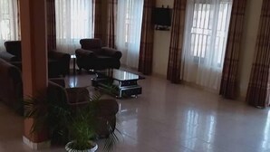 A spacious lobby with a tiled floor, several sofas, a television mounted on the wall, and large windows with curtains. - Kiboga Resort Hotel (Kiboga)