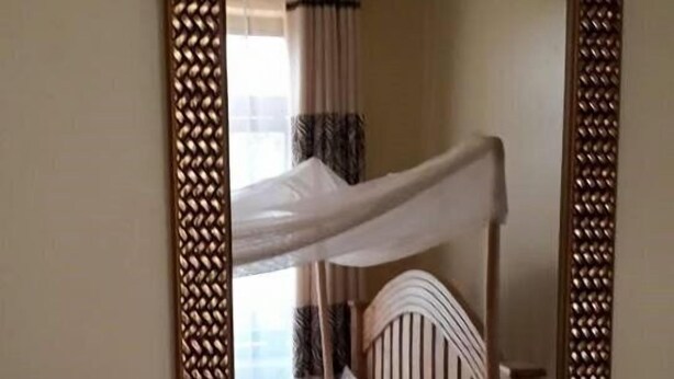 A bunk bed with a wooden headboard and white bedding, framed by a decorative mirror with a woven pattern. - Kiboga Resort Hotel (Kiboga)