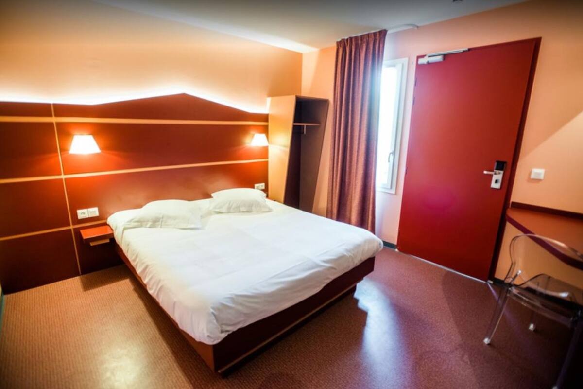 Een hotelkamer met een groot bed, nachtkastje, lamp, kledingkast en stoel.