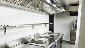 Een professionele keuken met roestvrijstalen werkbladen, een afzuigkap en betegelde vloer.