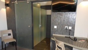 Een moderne badkamer met een douchecabine van glas, een klein bureau met stoel, en een aanrechtblad met een hondentandpatroon.